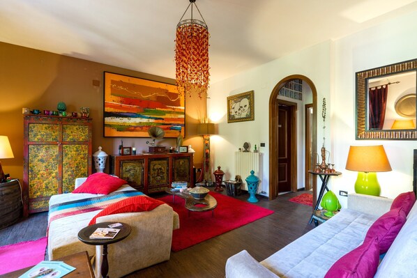 Una sala de estar acogedora con un sofá, un tapete rojo, una mesa de centro, una estantería y un cuadro en la pared.