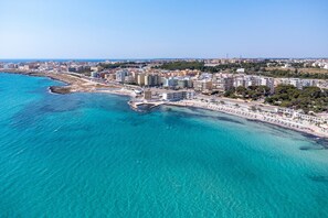 Vue aérienne d’une ville côtière avec une plage, des bâtiments et une eau d’un bleu limpide.