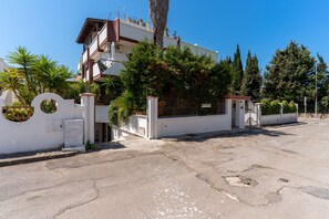 Un immeuble à plusieurs étages, doté d’une entrée fermée par un portail, entouré d’arbres et surplombant un ciel dégagé.