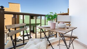 A balcony with a wooden table, a bench, a potted plant, and a white car parked outside.