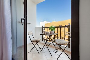 A balcony with a table, two chairs, a potted plant, and a view of buildings.