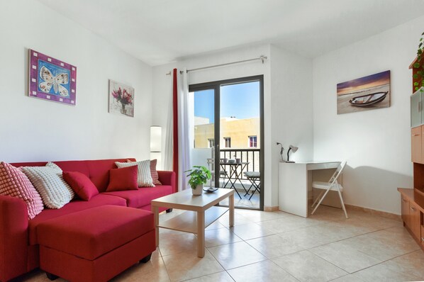 A red sofa, a small table with a plant, a desk with a chair, and a balcony with a view.