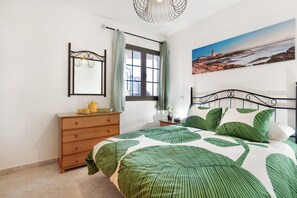 A bedroom with a bed, dresser, window, and a painting on the wall.
