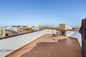A rooftop terrace with a view of the city, a table with chairs, and a railing.