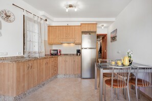 Une cuisine moderne avec des meubles en bois, un réfrigérateur en acier inoxydable, une table à manger avec des chaises et une horloge au mur.