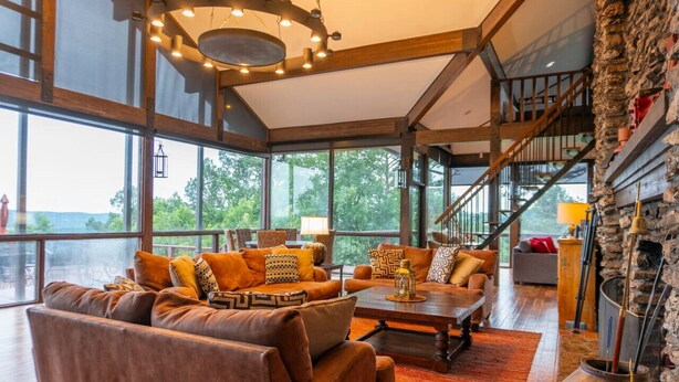 A spacious living room with leather sofas, a coffee table, and a fireplace. Large windows offer a view of the outdoors.
