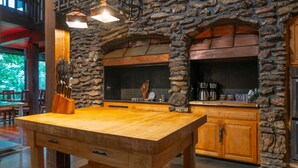 A rustic kitchen with a stone wall, wooden cabinets, and a large wooden table.