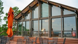 A modern building with large glass windows, outdoor seating with metal chairs and tables, and an orange umbrella.