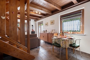 A dining area with a wooden staircase, a sofa, a dining table with chairs, and a window with curtains.
