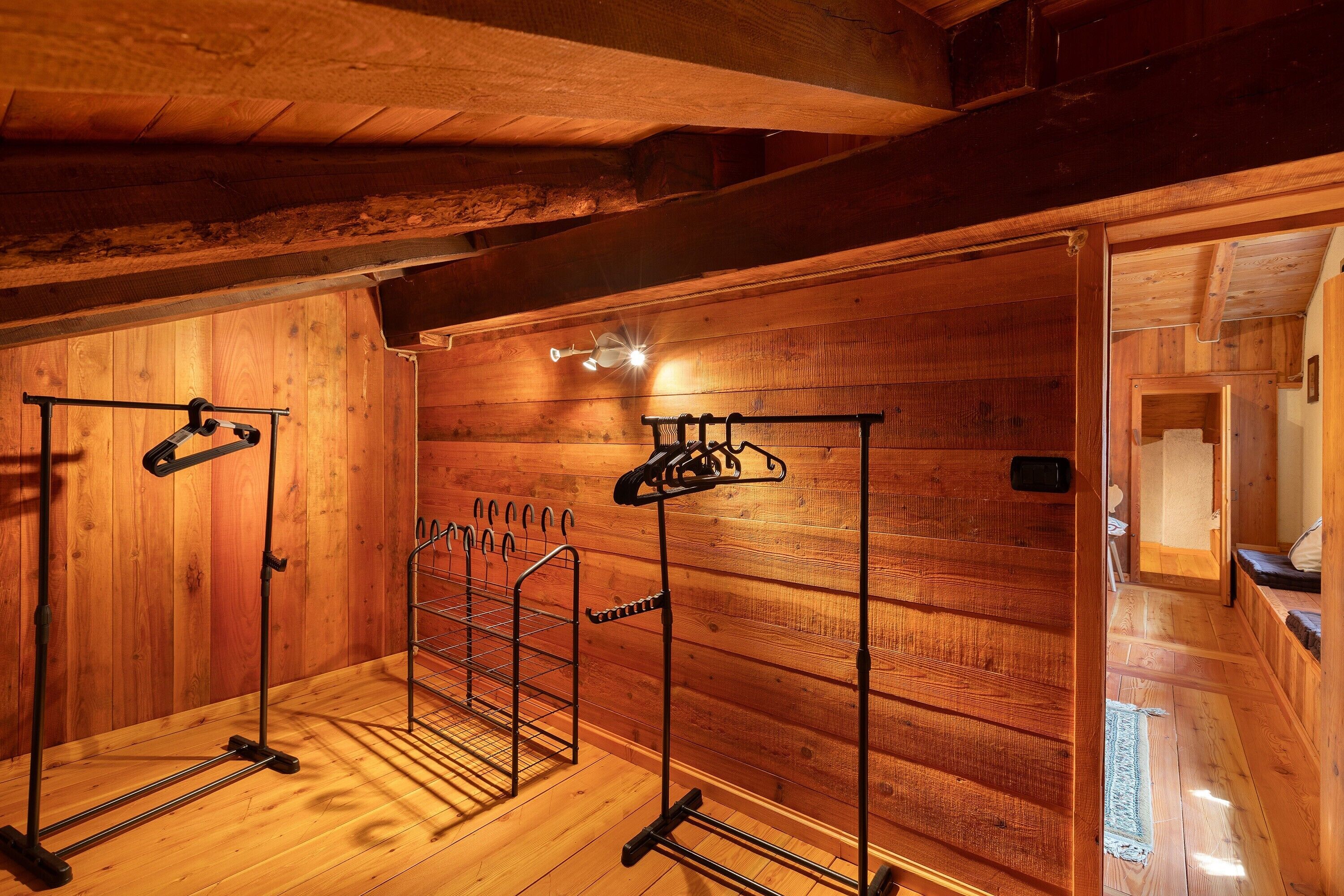Ein Holzinnenraum mit Holzbalkendecke, einer an der Wand befestigten Wäscheständer und einer sichtbaren Tür zu einem anderen Raum.