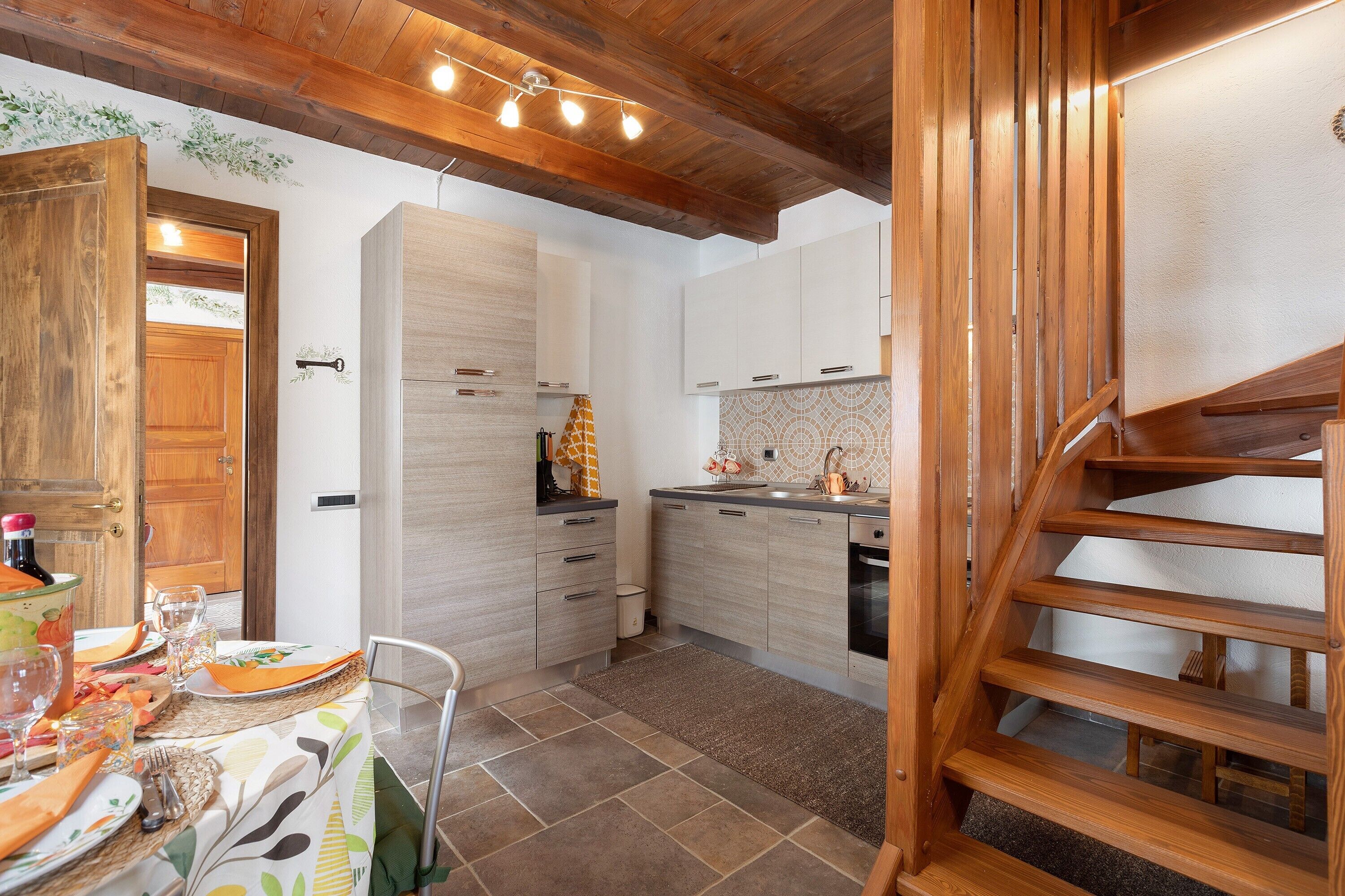 Une cuisine avec des meubles en bois, une table à manger dressée avec des assiettes et des verres, et un escalier menant à un autre niveau.