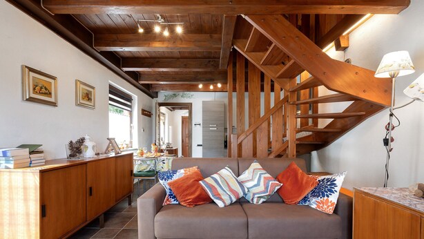 Ein Wohnzimmer mit braunem Sofa, einer Holztreppe und einem Essbereich mit Tisch und Stühlen.