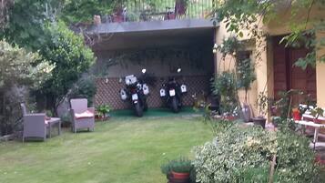 En trädgård med en gräsmatta, krukväxter och en rad uppställda motorcyklar.