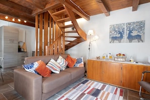 A modern living room with a wooden staircase, a sofa with patterned cushions, a wooden cabinet, and a wall art piece.