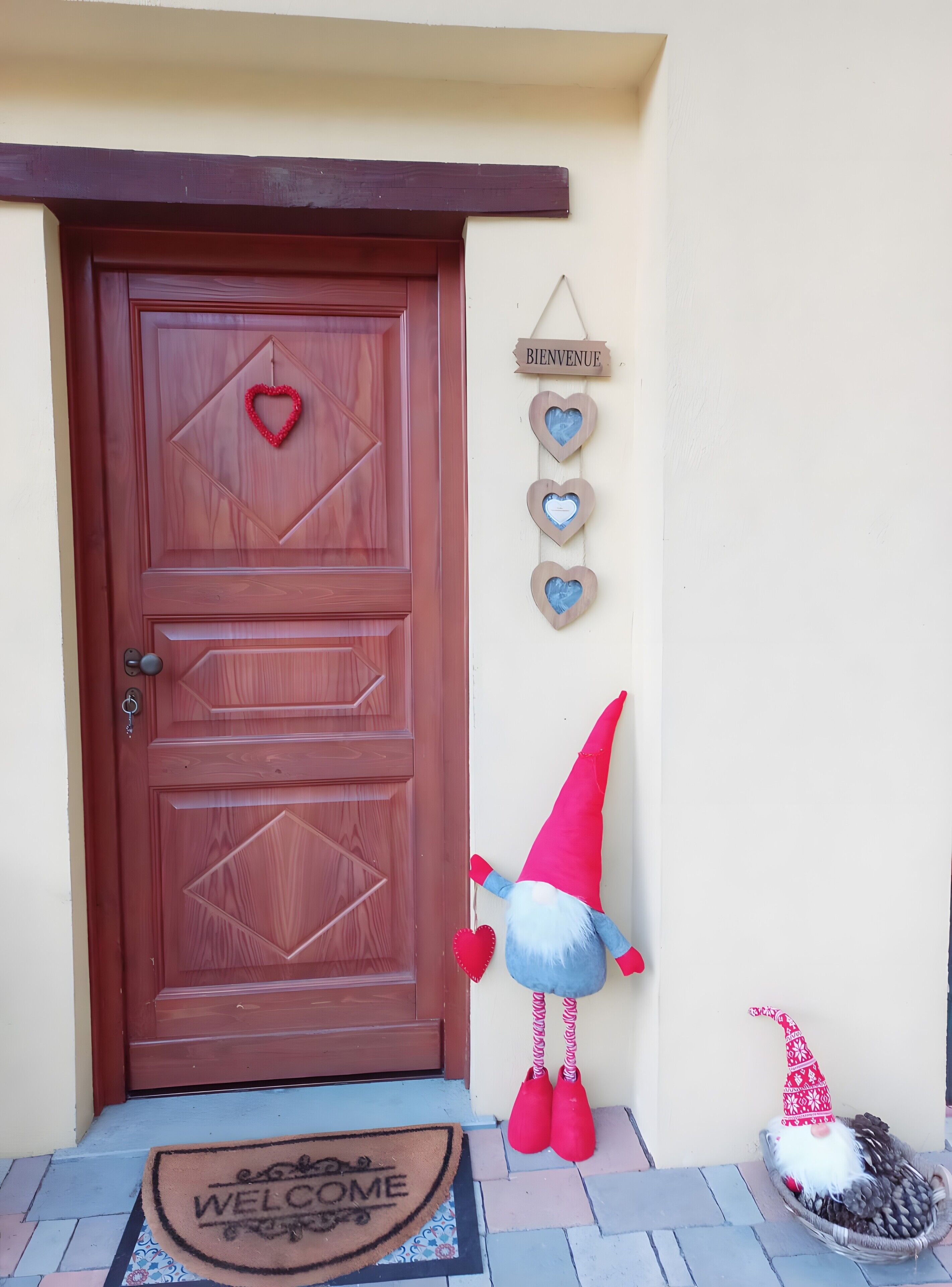 A wooden door with a heart decoration, a 'BIENVENUE' sign, and a gnome figure on the porch.