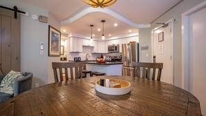 A modern kitchen with white cabinets, stainless steel appliances, and a wooden dining table with a central white island.