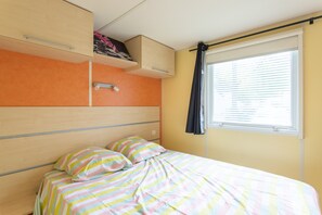 Un dormitorio con cama, ventana con persianas, estante con un cuadro y una puerta.