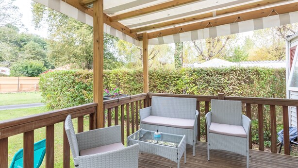 Una terraza cubierta con mobiliario de mimbre, una mesa de vidrio y vistas al jardín.