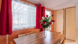 Un comedor con una mesa de madera, cortinas rojas y un jarrón con flores.