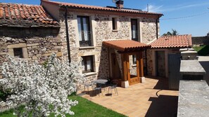 A stone building with a tiled roof, a patio with a table and chairs, and a flowering tree. - Country House 'Montes De Alhama' with Mountain View, Shared Terrace and Wi-Fi (Villarraso)