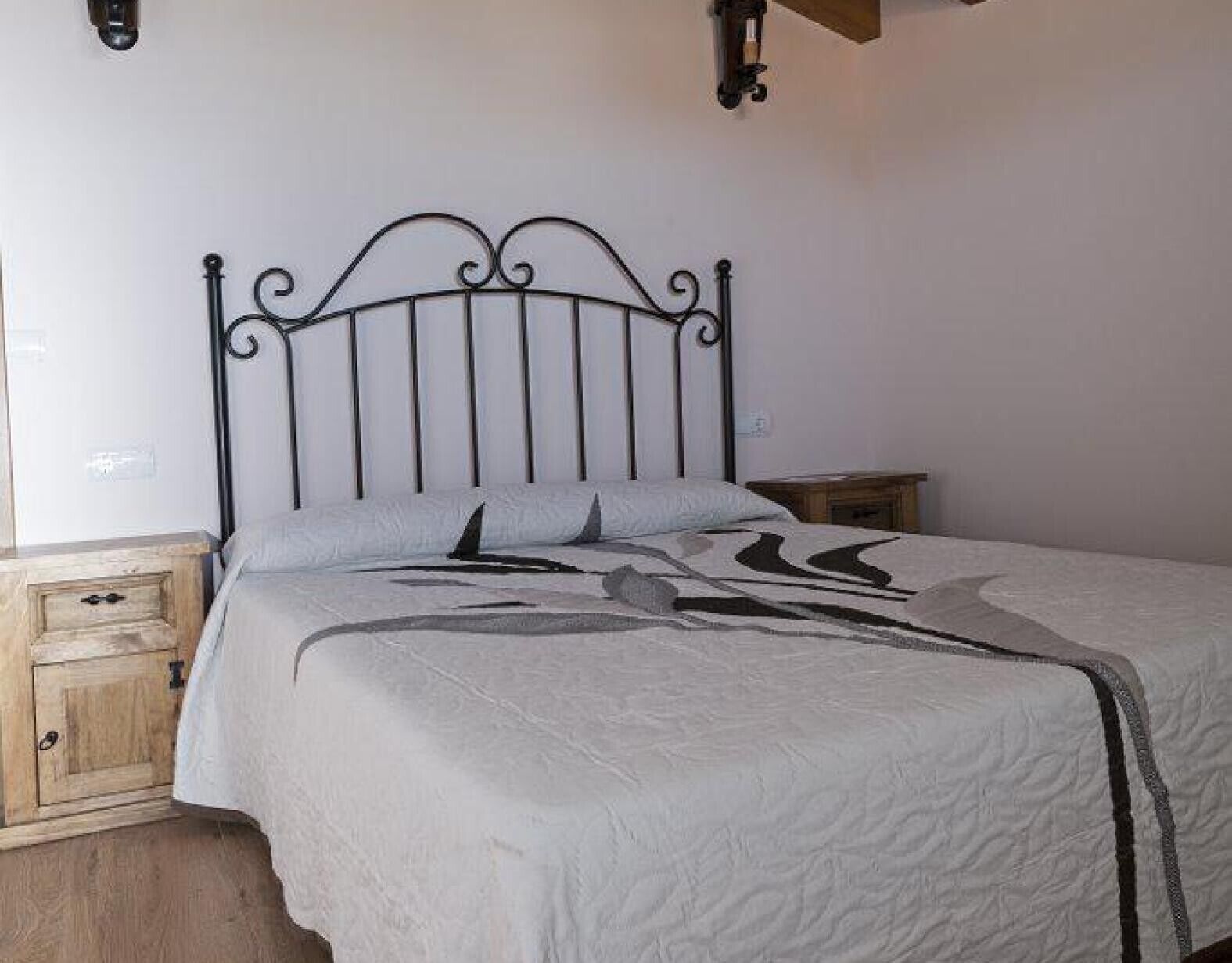 A bed with a metal frame, a wooden nightstand, and a wall-mounted light fixture.
