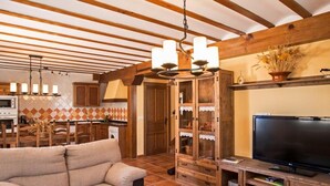 Una sala de estar con sofá, televisión, armarios de madera y una cocina al fondo.