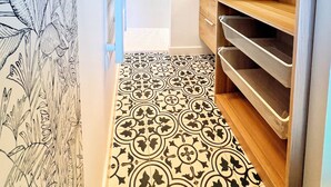 A narrow hallway with patterned flooring, a wooden closet with shelves, and a blue door.
