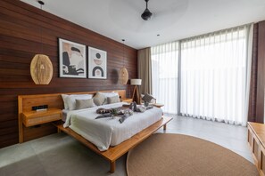 A modern bedroom with a wooden headboard, a large bed, a bedside table with a lamp, and artwork on the wall.