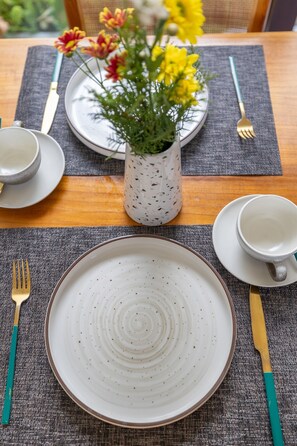 A table set with plates, bowls, and cutlery, a vase with flowers, and a placemat.