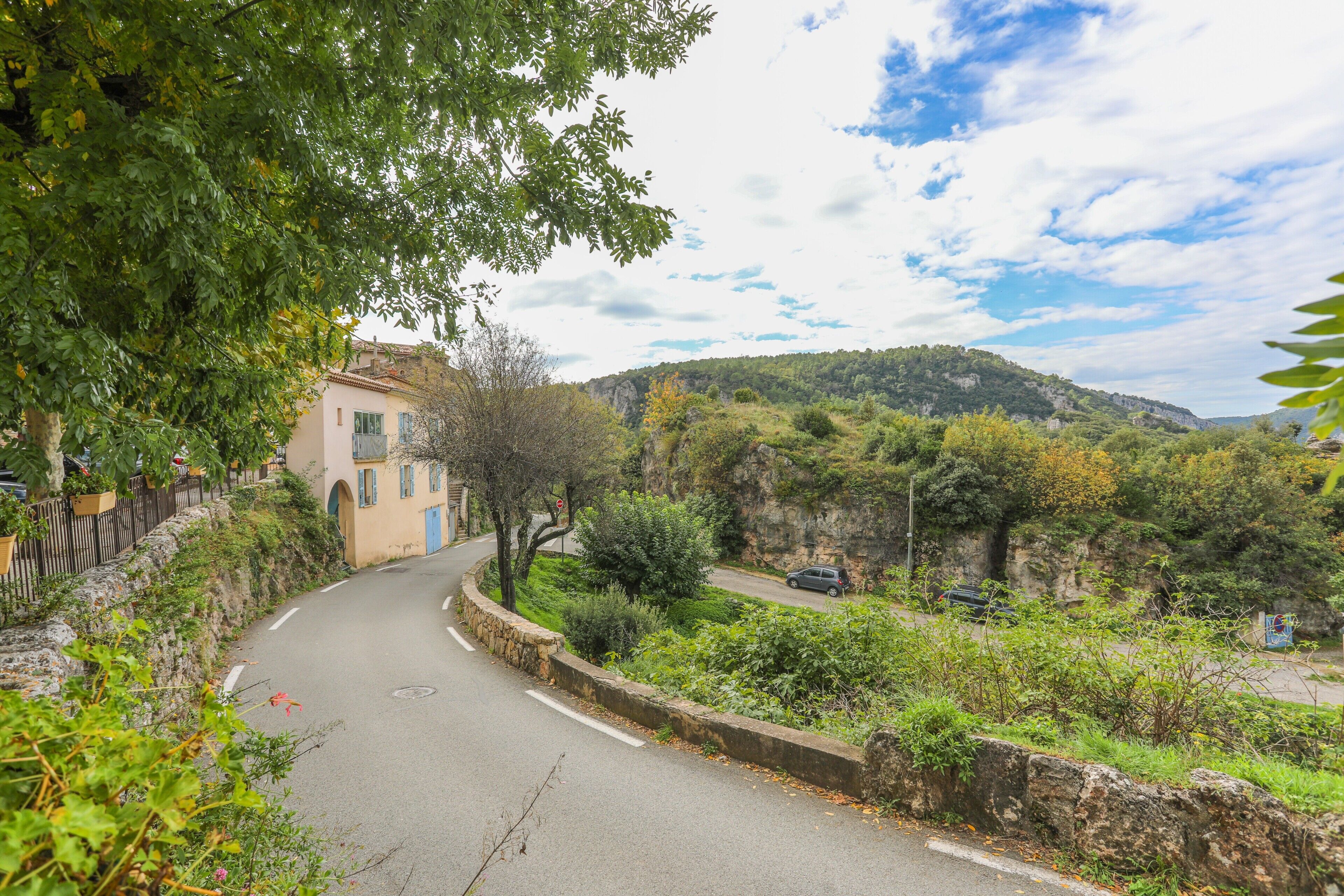 A winding road with a stone wall on one side and a building with a blue door.