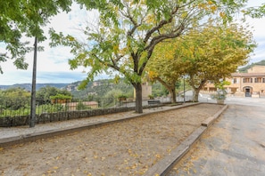 A paved pathway with trees and a fence, leading to a building with a tiled roof.