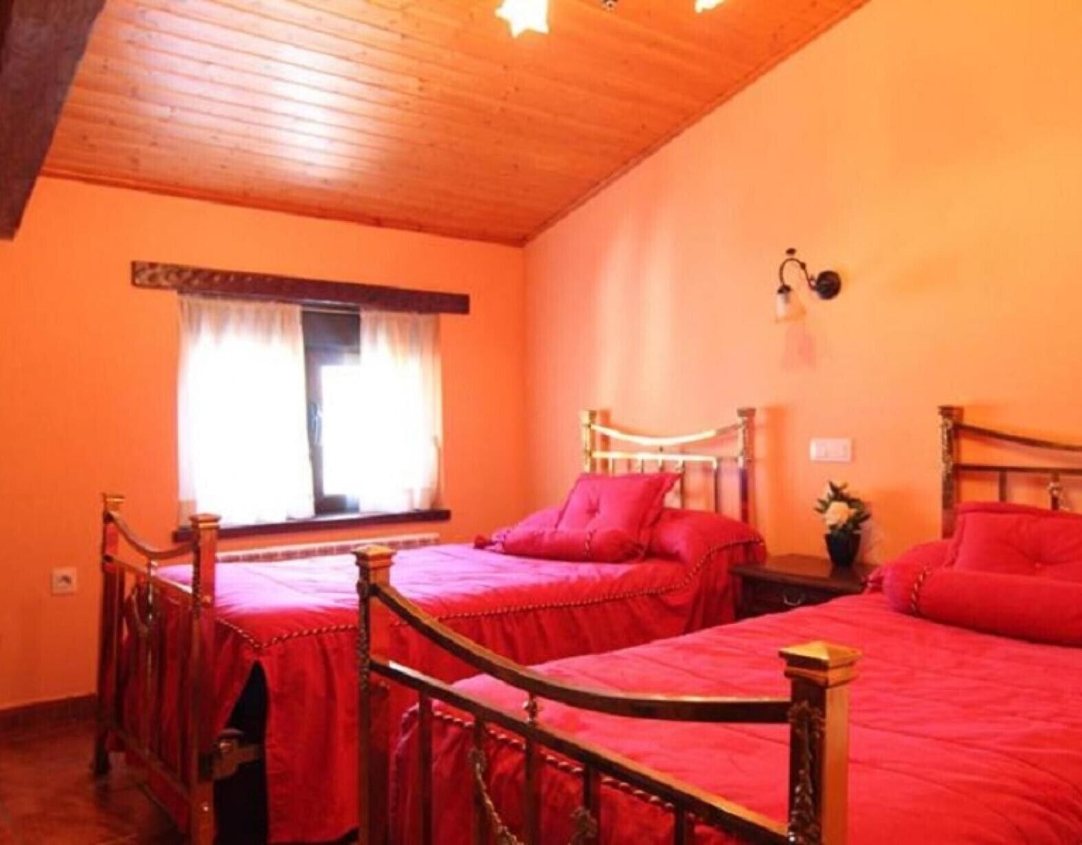 Une chambre avec deux lits, une fenêtre avec des rideaux, une lampe fixée au mur et un plafond en bois.