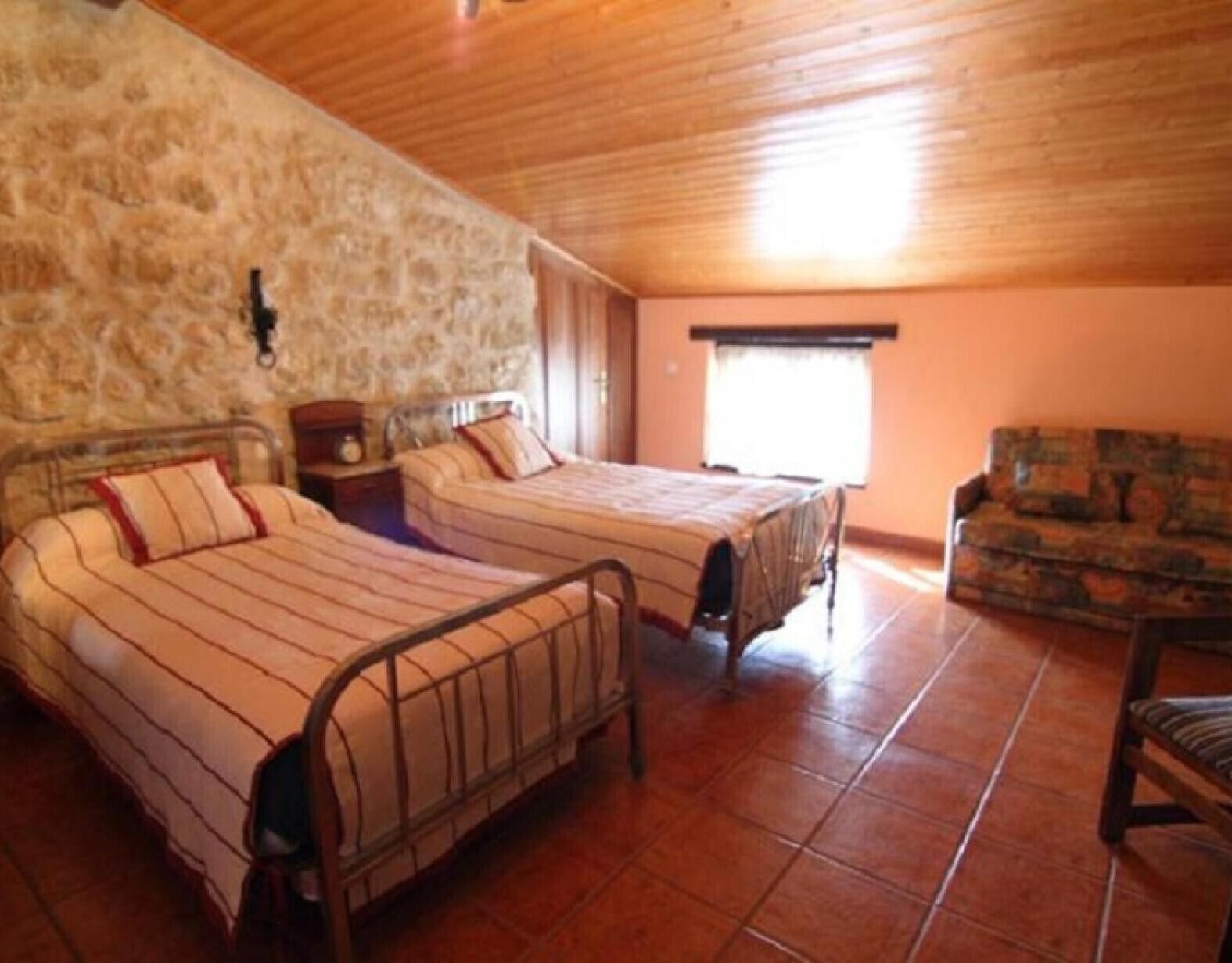 Quarto com duas camas, parede de pedra, teto de madeira e uma janela.