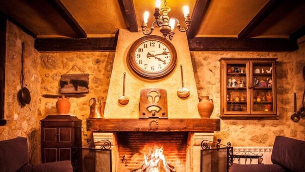 A cozy room with a fireplace, a clock, and a cabinet with decorative items. - Casa Rural El Manantial near Ciudad Rodrigo with Private Pool and Mountain Views (CIUDAD RODRIGO)