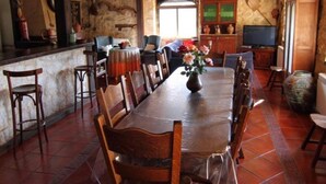 A dining area with a large wooden table, chairs, a vase with flowers, and a television in the background. - Casa Rural El Manantial near Ciudad Rodrigo with Private Pool and Mountain Views (CIUDAD RODRIGO)