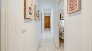 A hallway with framed artwork on the walls, a wooden door at the end, and a patterned table in the adjacent room. - Apartment 'La Fuente' with Balcony and Wi-Fi (El Paso)