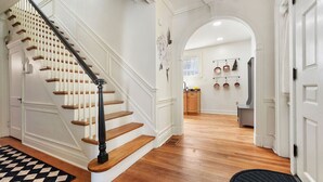A staircase with wooden steps and black balusters, leading to a kitchen area with wooden cabinets and a hanging pot rack. - ★ HostWise Stays ★ Charming Squirrel Hill Home with Garage, Near CMU (Pittsburgh)