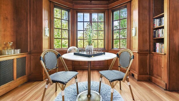 A corner room with wooden paneled walls, a round table with chairs, and a view through large windows. - ★ HostWise Stays ★ Charming Squirrel Hill Home with Garage, Near CMU (Pittsburgh)