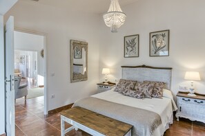 A bedroom with a large bed, two bedside tables with lamps, a chandelier, and framed botanical prints on the wall. - Holiday Home 'Ca La Yaya' with Mountain View, Wi-Fi and Air Conditioning (Llançà)