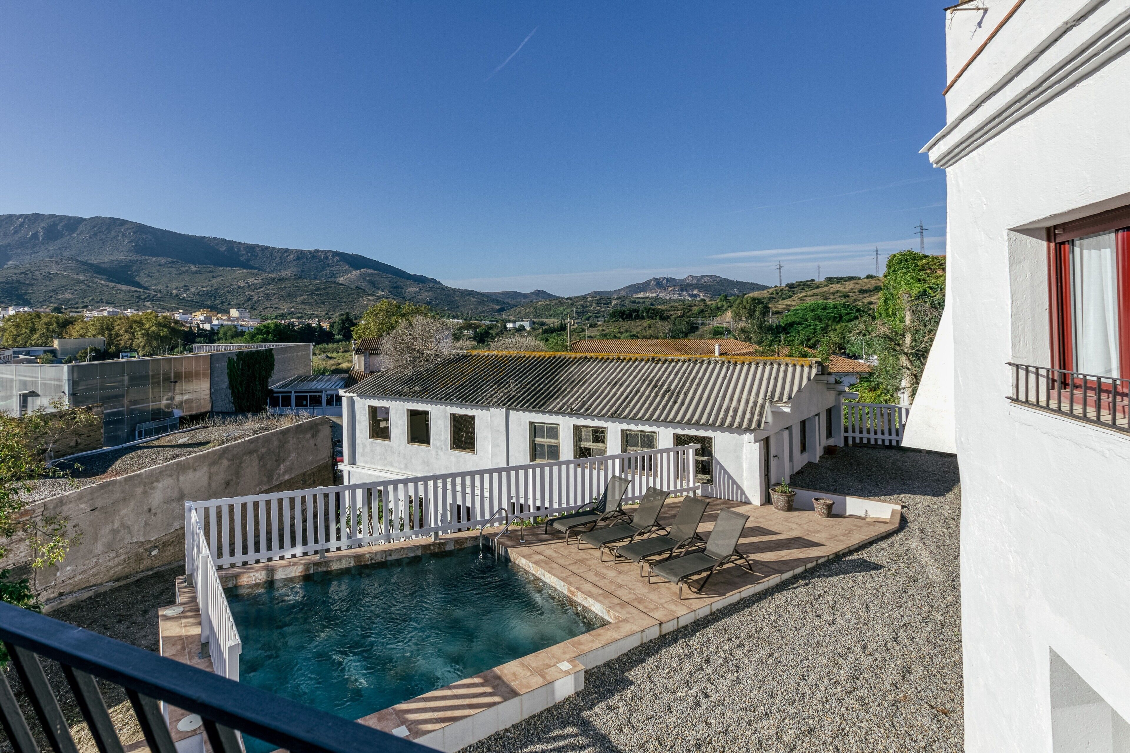 Zona de piscina con un edificio blanco, una valla blanca y vistas a la montaña.