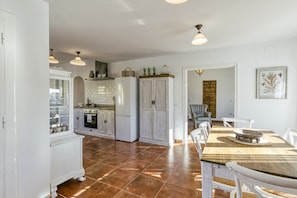 A kitchen with white cabinets, a dining table with chairs, and a view into the living area. - Holiday Home 'Ca La Yaya' with Mountain View, Wi-Fi and Air Conditioning (Llançà)