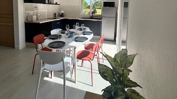 Eine moderne Küche mit weißen Schränken, einem Essbereich mit Tisch für vier Personen und einem großen Fenster für natürliches Licht.