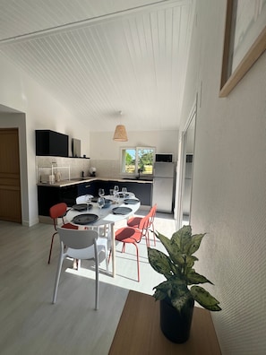 A modern kitchen with white cabinetry, a dining area with a table set for four, and a large window providing natural light. - Holiday Home 'Maison Proche Vendée Globe 6p' with Private Terrace and Air Conditioning (Sainte-Foy)