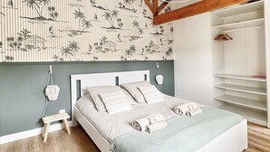 Ein Schlafzimmer mit Bett, einem hölzernen Hocker, einer Pendelleuchte, einem Kleiderschrank und einer Wand mit Streifenmuster.
