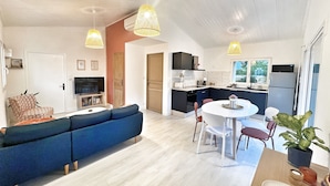 Ein modernes Interieur mit einer Couch, einem Esstisch, Stühlen, einer Küchenzeile und Pendelleuchten.