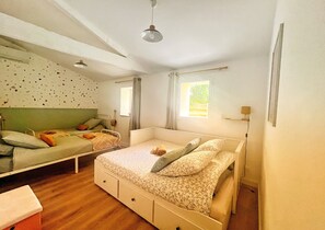 A bedroom with two single beds, a large bed, wooden flooring, a ceiling fan, and a window with curtains. - Holiday Home 'Maison Proche Vendée Globe 6p' with Private Terrace and Air Conditioning (Sainte-Foy)