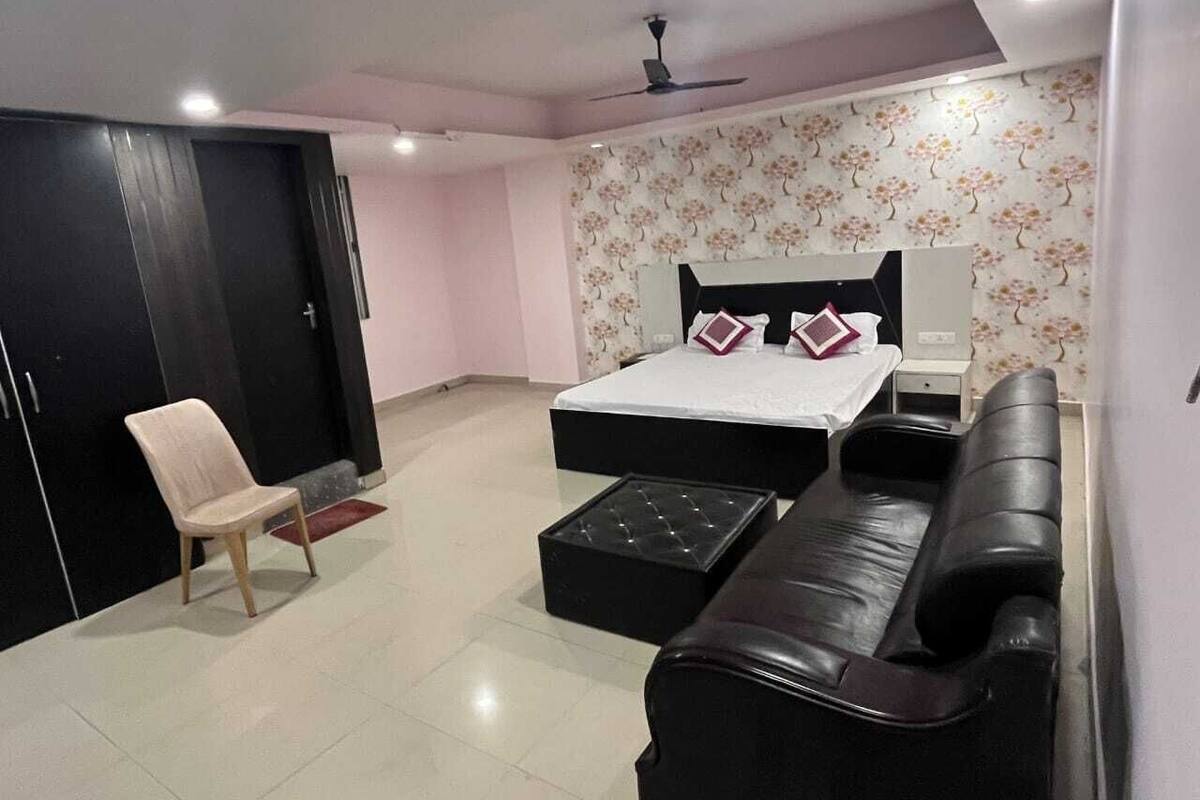A bedroom with a bed, a black leather sofa, a wooden chair, and a wardrobe.