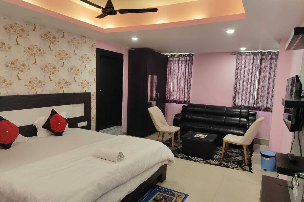 A bedroom with a bed, a black leather sofa, a small table, and a ceiling fan.