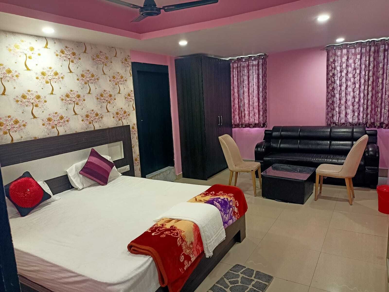 A bedroom with a bed, a black leather sofa, two chairs, a small table, and a wardrobe.