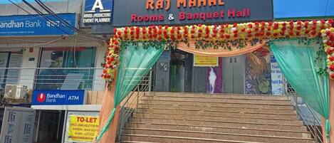 Un edificio con un letrero que indica Raj Mahal Rooms & Banquet Hall, una escalera y un cajero automático de Bandhan Bank.